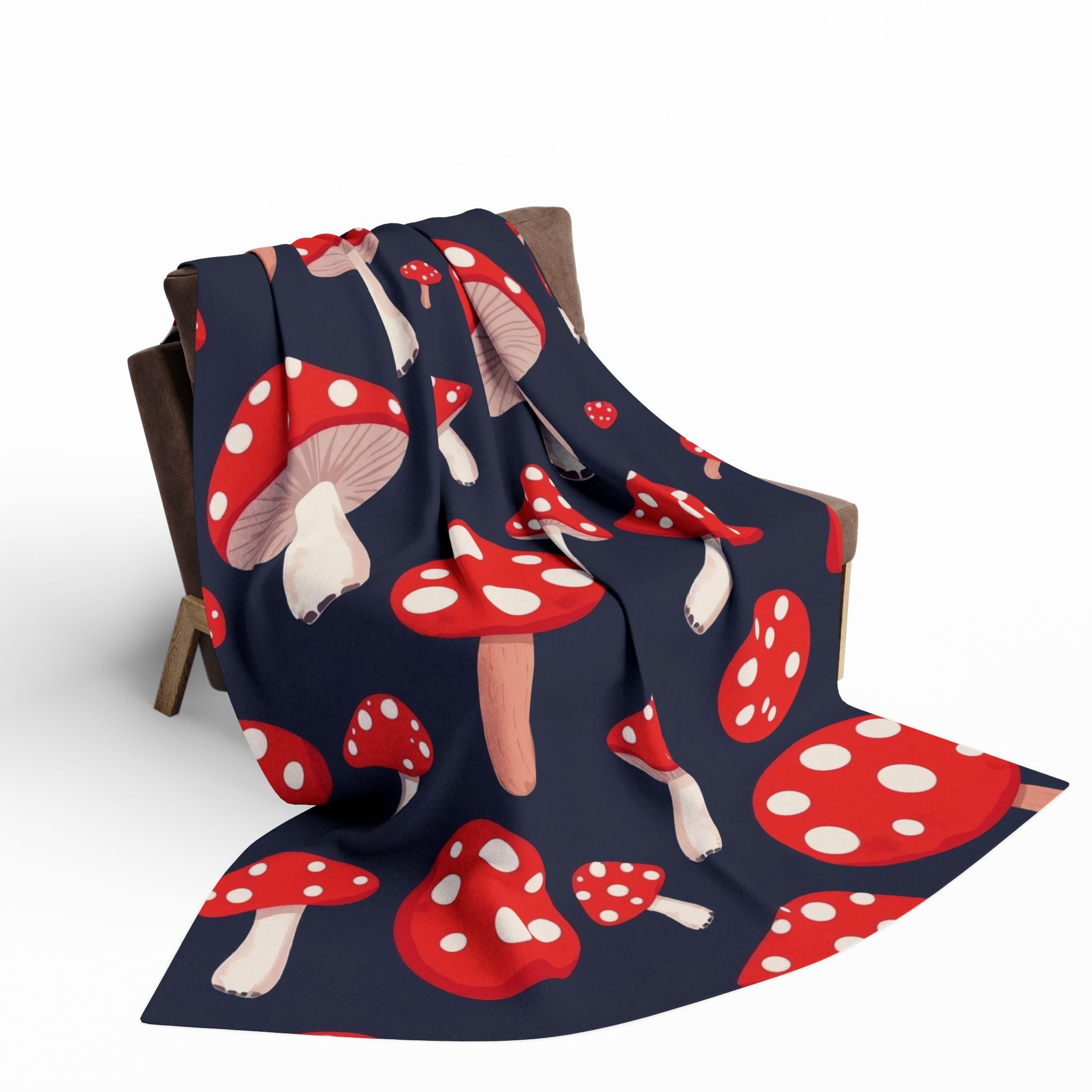 Fleece blanket with red and white mushroom pattern draped over a chair on a white background.