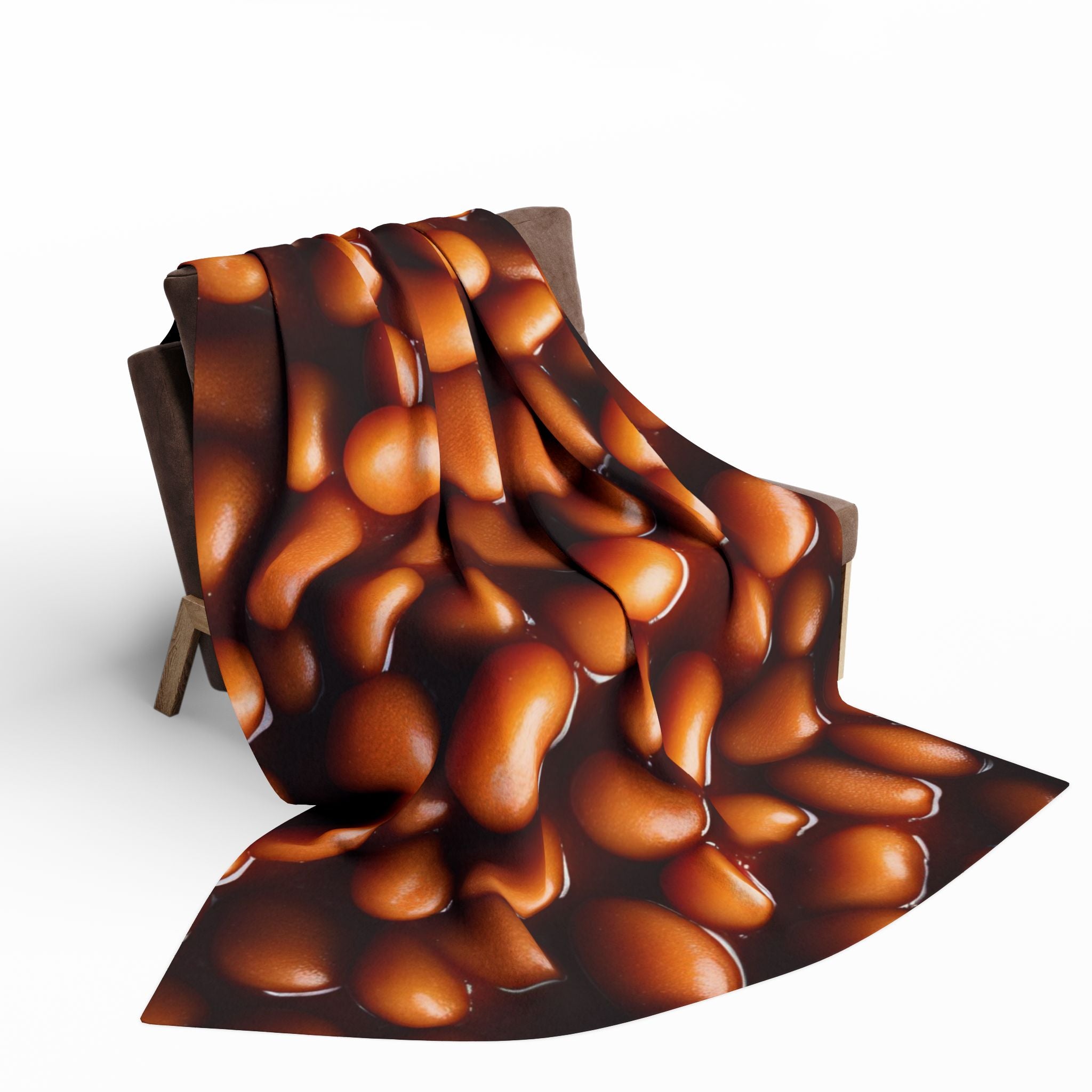 Printed fleece blanket of baked beans draped over a brown sofa on a white background.
