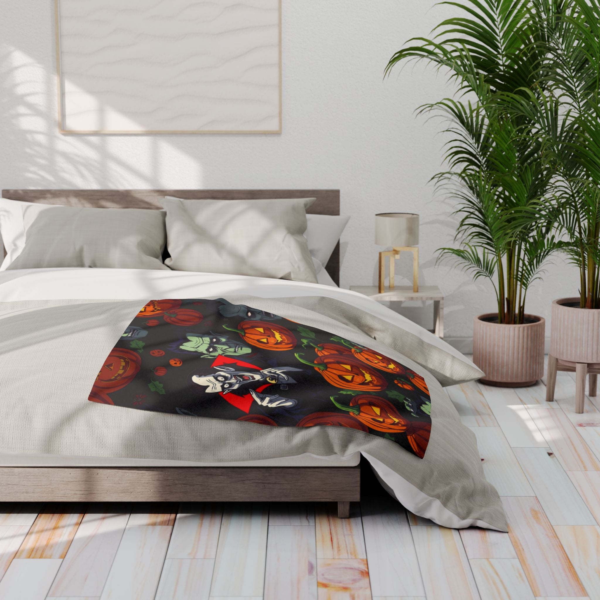 Bed with a decorative fleece blanket featuring pumpkin lanterns, vampire, Dracula and Frankenstein, in a bedroom setting with plants.